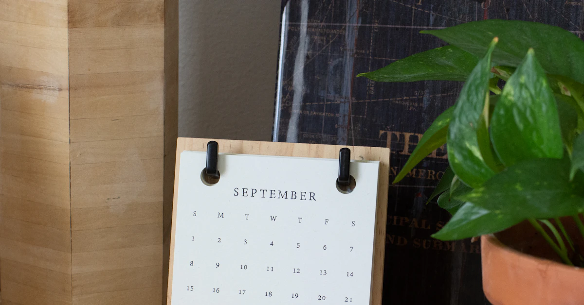 A desk calendar open on September beside a green plant.