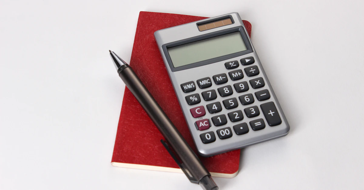 A calculator and a pen on a red notebook against a white surface — working out a cost.